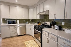 Une cuisine moderne avec des meubles blancs, un lave-vaisselle en acier inoxydable, un four à micro-ondes, une cuisinière et un grille-pain.