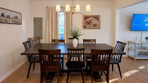 A dining room with a large table, six chairs, a chandelier, a vase with plants, a painting, and a television on the wall. - Spacious 4BR Family Home with Game Room (Raleigh)