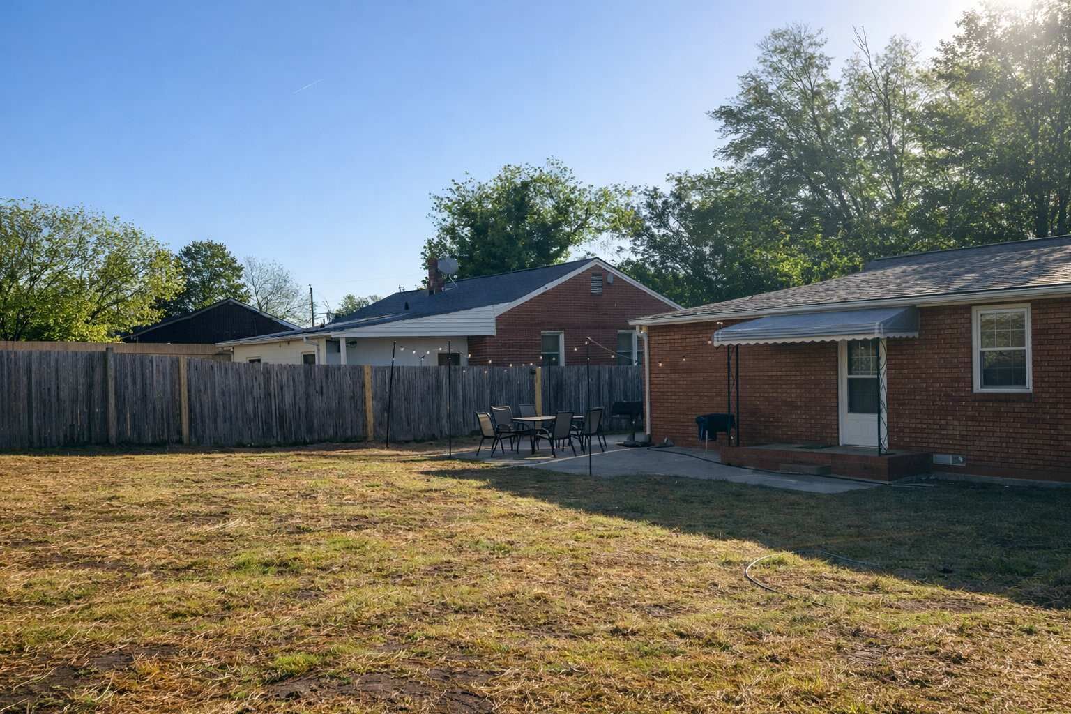 Un patio trasero con cerca de madera, un patio con sillas y un pequeño edificio de ladrillo.