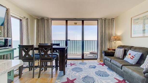 Ein Zimmer mit Esstisch, Stühlen, einer Couch, einem Fernseher und einem Balkon mit Blick.