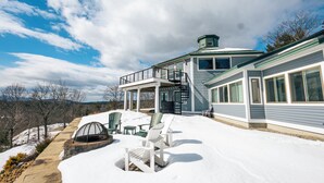 Ein Haus mit überdachter Terrasse, Sitzgelegenheiten im Freien und verschneiter Landschaft.