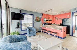 Ein kompakter Wohnraum mit Küchenbereich, einer Sitzecke mit gemustertem Sofa und einem an der Wand montierten Fernseher.