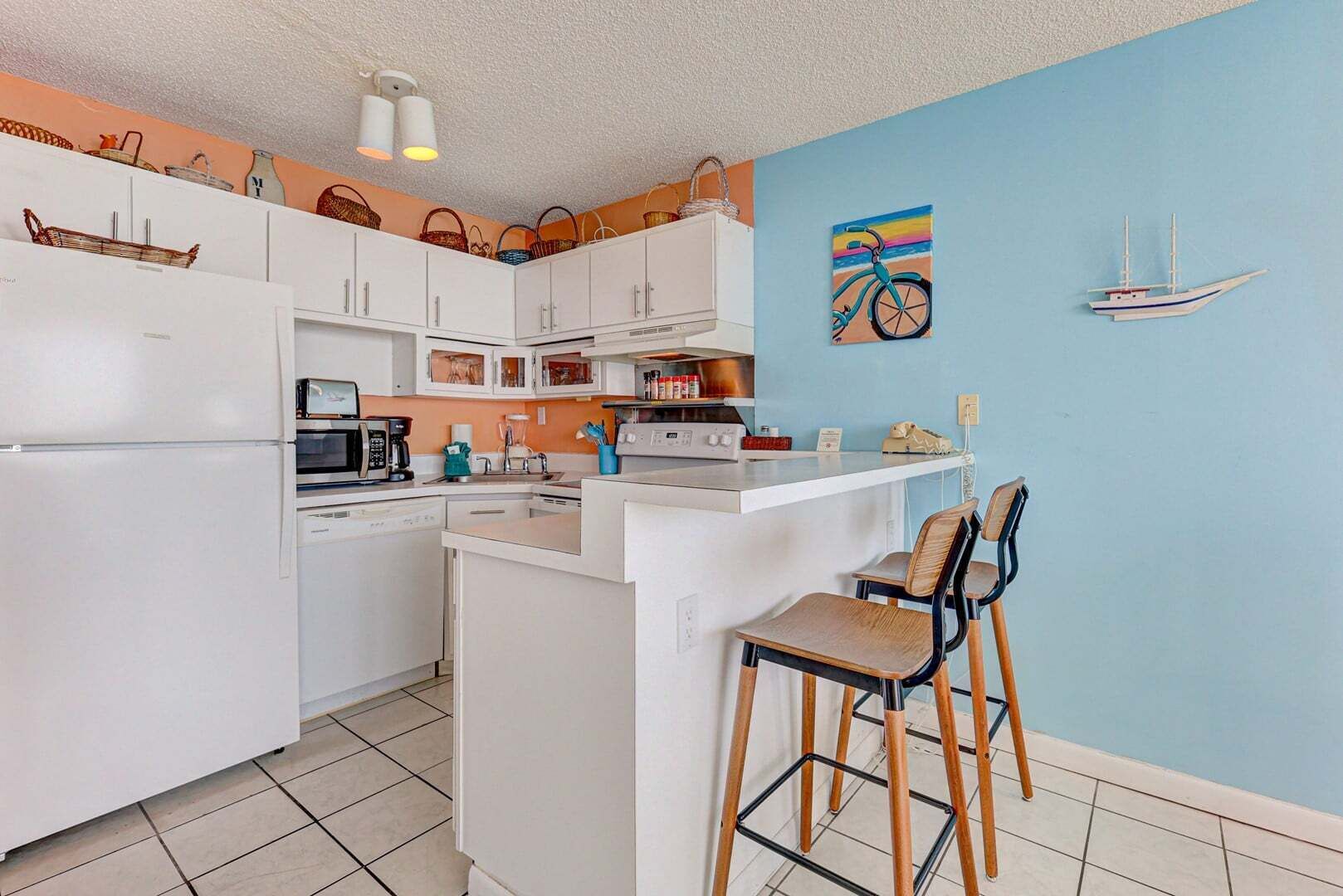 Cocina compacta con armarios blancos, una isla central, taburetes de bar y una pared de acento azul.
