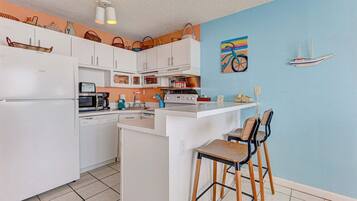 Cocina compacta con armarios blancos, una isla central, taburetes de bar y una pared de acento azul.