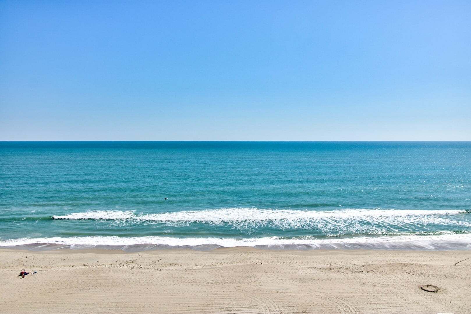 Una playa con cielo despejado, mar tranquilo y orilla arenosa.