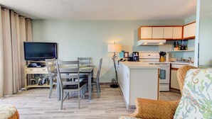 Un espacio habitable compacto con televisor, mesa de comedor, sillas, sofá, zona de cocina y lámpara.