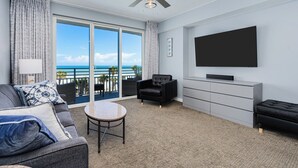 Ein modernes Hotelzimmer mit Balkon, Flachbildfernseher, Sofa, Sessel und kleinem Tisch.