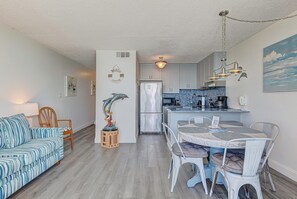 A modern kitchen with white cabinets, a refrigerator, and a dining area with a table and chairs. - Oceanfront charm at 1008 Blue Dolphin, a cozy 1-bedroom in Carolina Beach. (Carolina Beach)