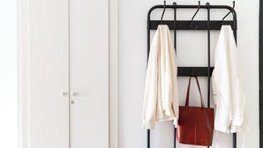Une porte blanche, un banc en métal noir et un portant à vêtements avec un sac rouge et des vêtements blancs.