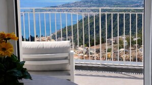 Ein Balkon mit Blick auf eine Küstenlandschaft, eine weiße gepolsterte Bank und ein Blumentopf.
