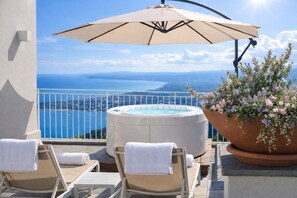Ein Balkon mit Whirlpool, Liegestühlen, Sonnenschirm und Blumentopf.
