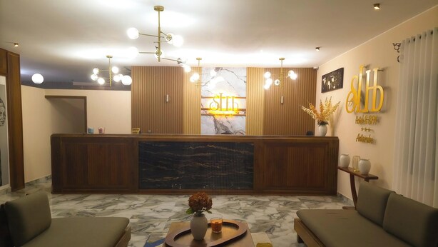 Zona de recepción de hotel con mostrador de mármol, paneles de madera, un espejo grande y una señalización en el mostrador.