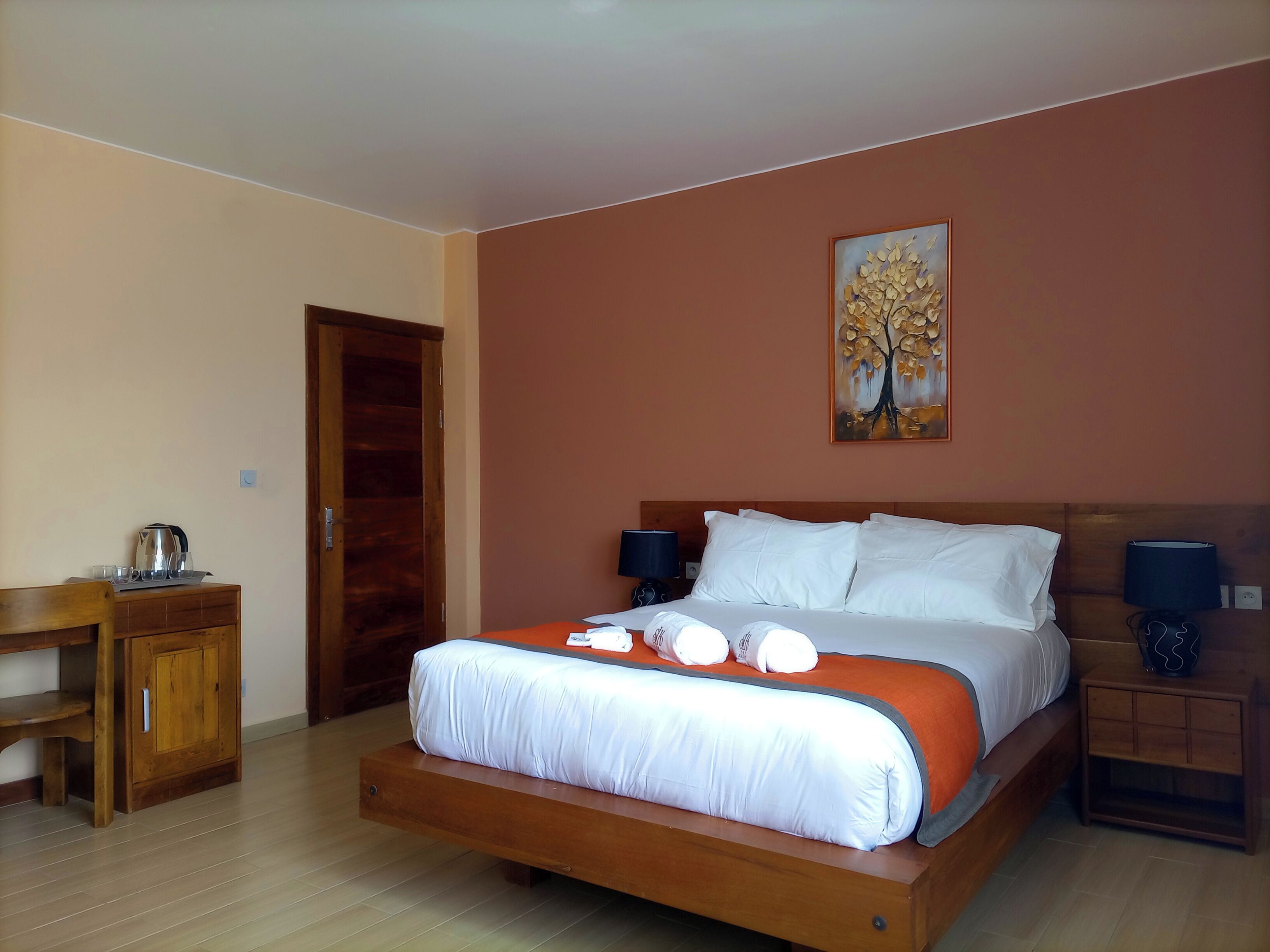 A bedroom with a bed, bedside tables, a wooden desk, and a door.