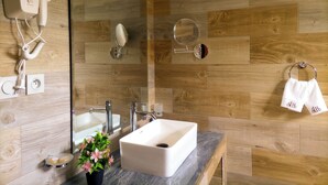 Un baño con pared de madera, un lavamanos blanco, un espejo, un perchero para toallas y un secador de pelo.