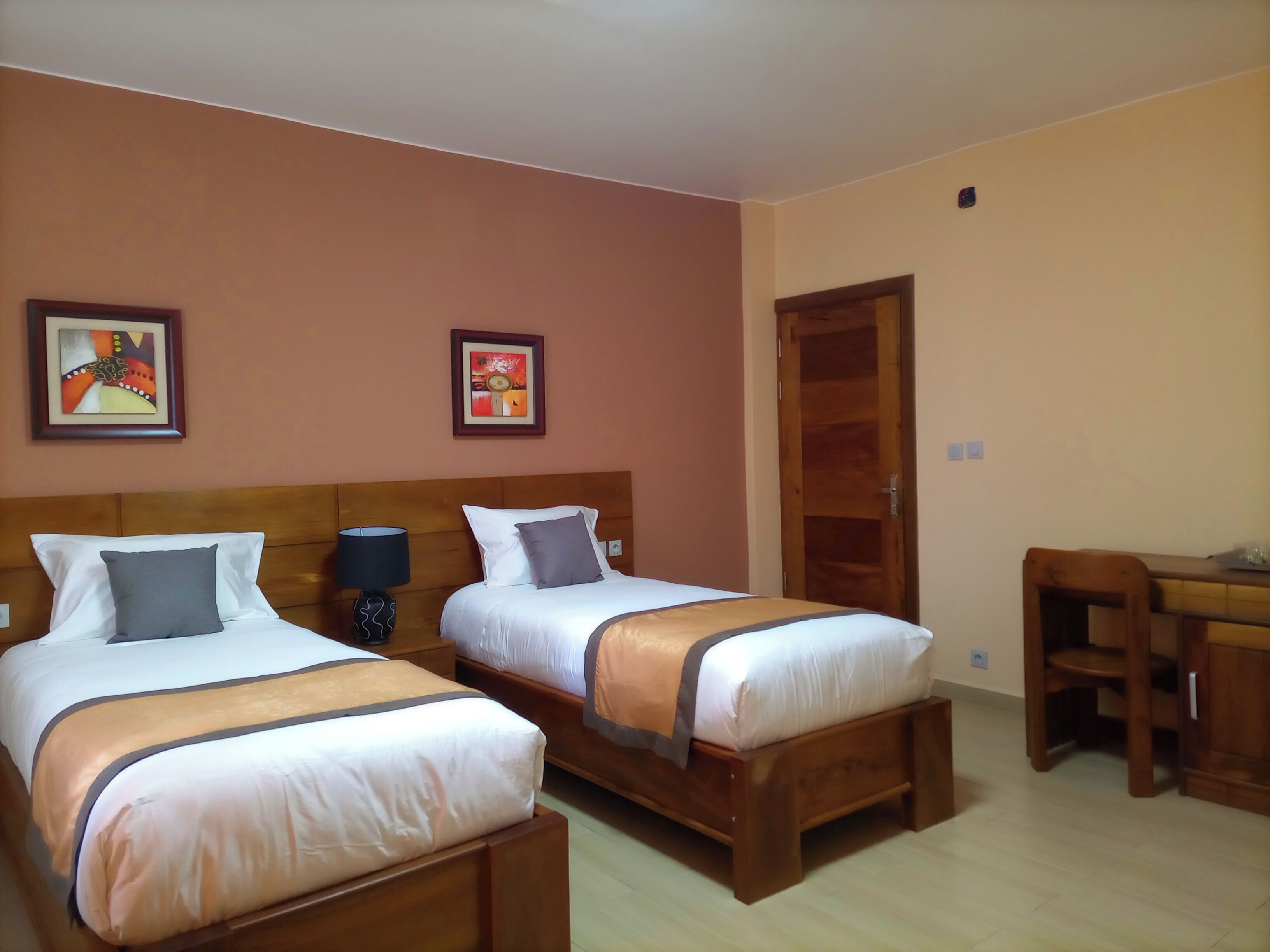 A hotel room with two beds, a wooden headboard, a desk, and two framed pictures on the wall.