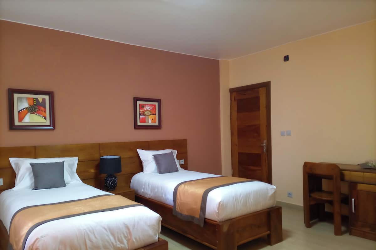 A hotel room with two beds, a wooden headboard, a desk, and two framed pictures on the wall.