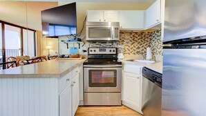A compact kitchen with a microwave, stove, oven, dishwasher, and a large refrigerator. - Charming 1-bedroom oceanfront condo in Carolina Beach, perfect for 4 guests! (Carolina Beach)