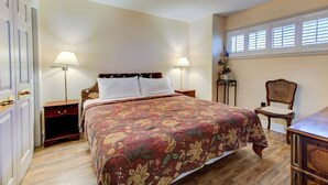 A bedroom with a bed, two bedside tables, a nightstand, a chair, a window with blinds, and a door. - Charming 1-bedroom oceanfront condo in Carolina Beach, perfect for 4 guests! (Carolina Beach)