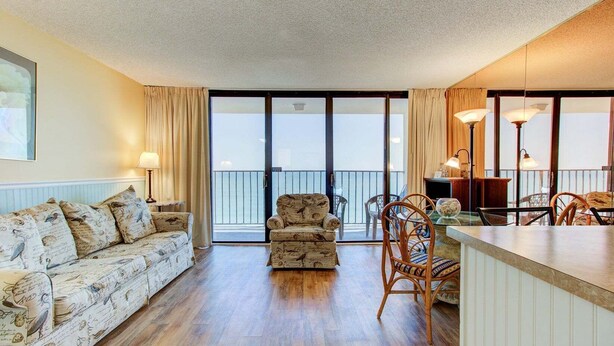 A living room with a sofa, armchair, and dining area with chairs and a table. - Charming 1-bedroom oceanfront condo in Carolina Beach, perfect for 4 guests! (Carolina Beach)