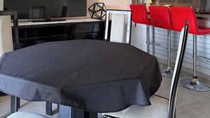 Zona pranzo con tavolo, sedie, televisore e angolo cottura con pensili e piano di lavoro.