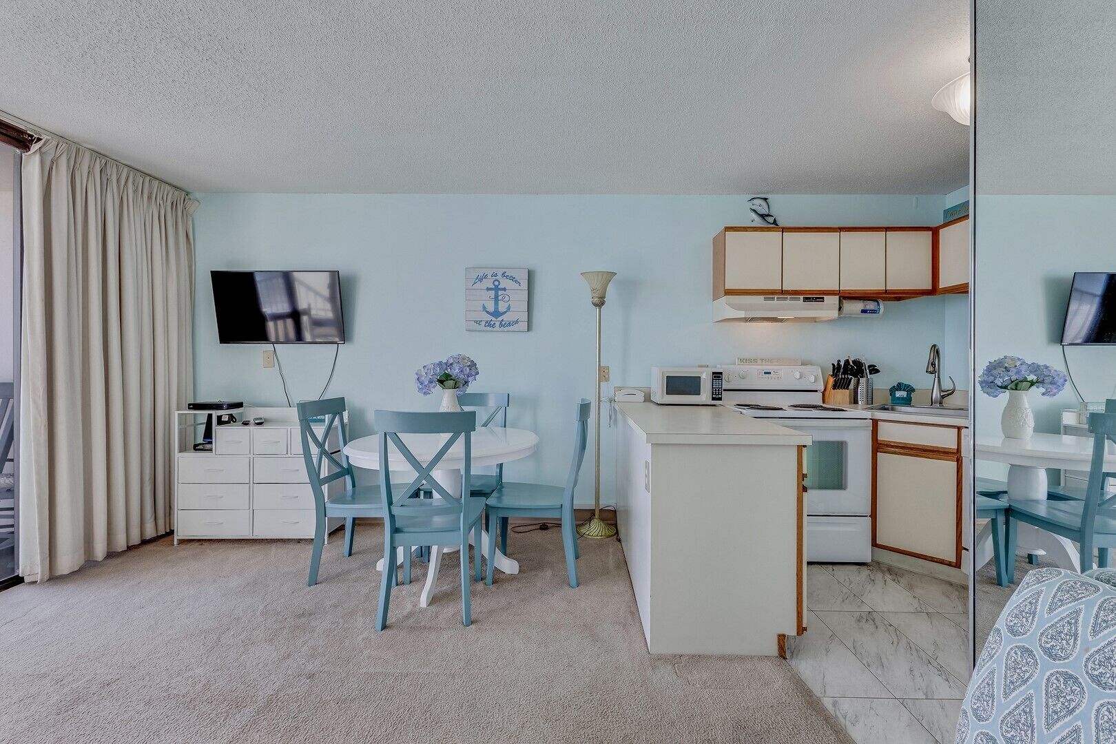 Cocina compacta con comedor, televisor de pantalla plana y una pequeña isla con microondas.