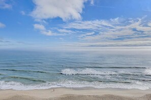 Ein Strand mit Wellen, blauem Himmel und einer Person, die spazieren geht.
