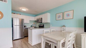 A kitchen with white cabinets, a stainless steel refrigerator, a microwave, and a dining table with chairs. - Stunning 1 Bedroom Oceanfront Condo in Carolina Beach 1106 (Carolina Beach)