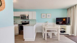 A compact kitchen with a microwave, oven, and sink, a dining area with a table and chairs, and a TV in a corner. - Stunning 1 Bedroom Oceanfront Condo in Carolina Beach 1106 (Carolina Beach)