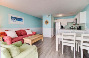 Ein kompakter Wohnbereich mit Küchenzeile, einem roten Sofa, einem grünen Sessel und einem Esstisch.