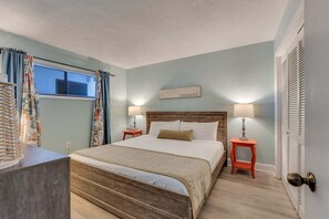 A bedroom with a wooden bed, two bedside tables with lamps, a window with curtains, and a sign on the wall. - Experience oceanfront luxury at 1108 Ocean Serenity, Carolina Beach. (Carolina Beach)