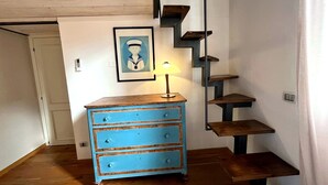 Une pièce avec une commode bleue, un tableau encadré au mur et un escalier.