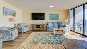 A living room with a sofa set, a coffee table, a TV, and a large window. - Stunning oceanfront 2-bedroom condo at Carolina Beach 1110 (Carolina Beach)