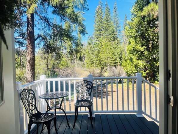 A wooden deck with a white railing, two metal chairs, and a small round table.