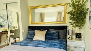 A bedroom with a bed, a desk, a chair, a mirror, a lamp, and a potted plant. - Dafna, Unit 3 - Two bedroom/1 Bath stylish home (Cromberg)