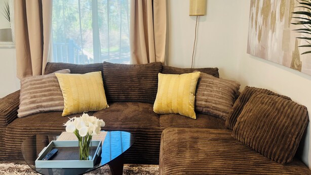 A living room with a brown sofa, yellow cushions, a glass coffee table with a remote control, and a vase of white flowers. - Dafna, Unit 3 - Two bedroom/1 Bath stylish home (Cromberg)