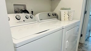 A laundry area with a front-loading washer and dryer, a utility sink, and a laundry basket on the counter. - Dafna, Unit 3 - Two bedroom/1 Bath stylish home (Cromberg)