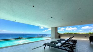 Un espace aménagé au bord de la piscine, avec des chaises longues et une vue sur l’océan.
