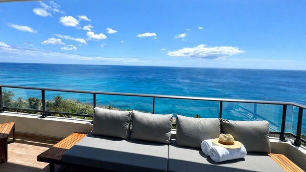 Un balcon avec vue sur l’océan, un canapé avec des coussins, un chapeau et des serviettes.