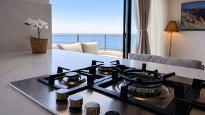 Une cuisine moderne équipée d’une cuisinière à gaz, avec vue sur la mer, une orchidée en pot et un canapé agrémenté de coussins.