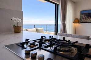 Eine moderne Küche mit Gaskochfeld, Meerblick, einer Topfpflanze und einer Couch mit Kissen.