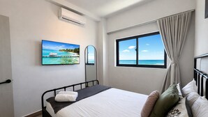 Une chambre d’hôtel équipée d’un lit, d’une télévision, d’une fenêtre donnant sur l’océan et d’un appareil de climatisation.