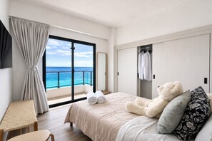 Een hotelkamer met een bed, een grote knuffelbeer, een bankje en uitzicht op de oceaan.