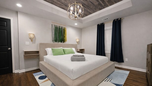 Una camera da letto con un letto, comodini, un lampadario, un'opera d'arte a parete e una finestra con tende.