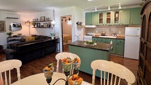 A modern kitchen with green cabinets, a central island, and a dining area with white chairs.