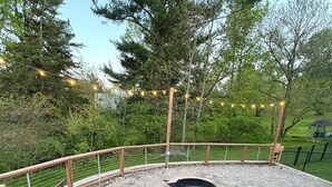 A circular stone deck with a fire pit, wooden railings, and string lights.