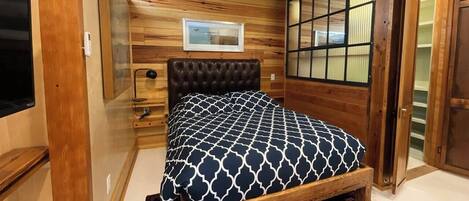 A wooden-paneled room with a bed, a bedside table, a framed picture, and a sliding door.