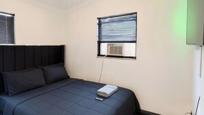 Et soveværelse med seng, ventilator, et vindue med persienner og en aircondition.
