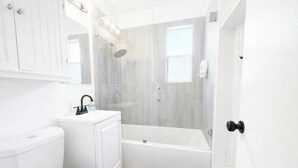 Et badeværelse med toilet, håndvask, bruser og badekar.