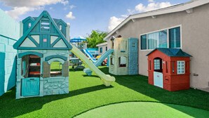 Ein Kinderspielbereich mit verschiedenen Spielgeräten, darunter Rutschen und Kletterwänden, umgeben von Gebäuden.