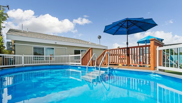 Ein klarer, blauer Swimmingpool mit Holzterrasse und Stufen, umgeben von einem weißen Zaun.
